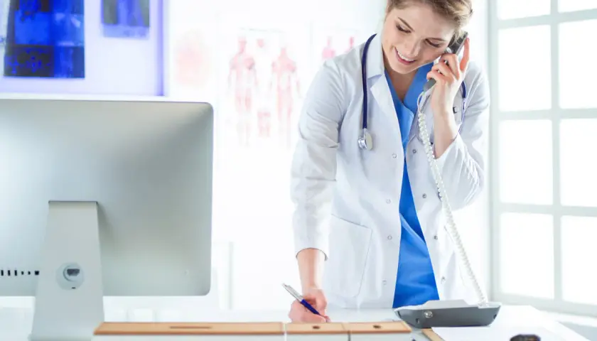 Medico al telefono, impegnato nella gestione appuntamenti, mentre scrive su un blocco note.