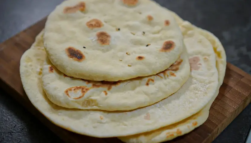 Pile de pains arabes moelleux, légèrement dorés par la cuisson, sur une planche en bois. Parfait pour accompagner un repas.