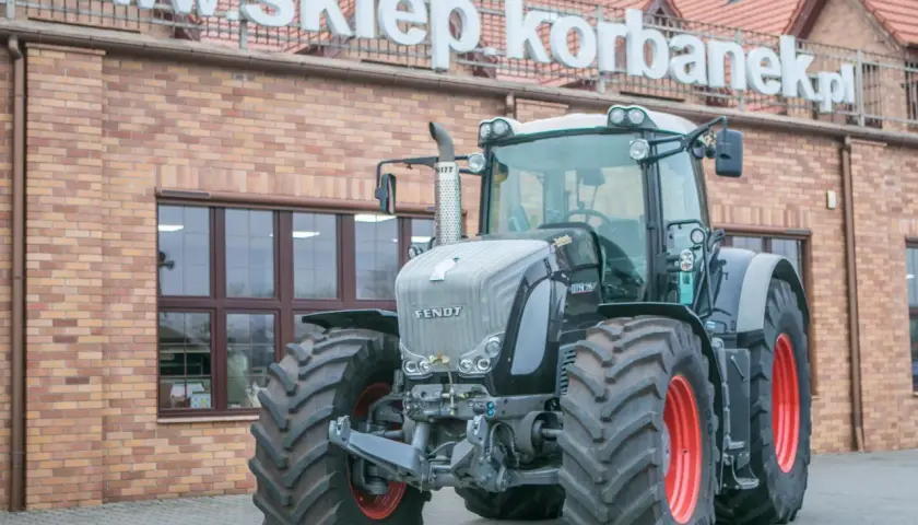 Potężny Fendt 936 Vario, gotowy do pracy na polu, przed budynkiem sklepu.