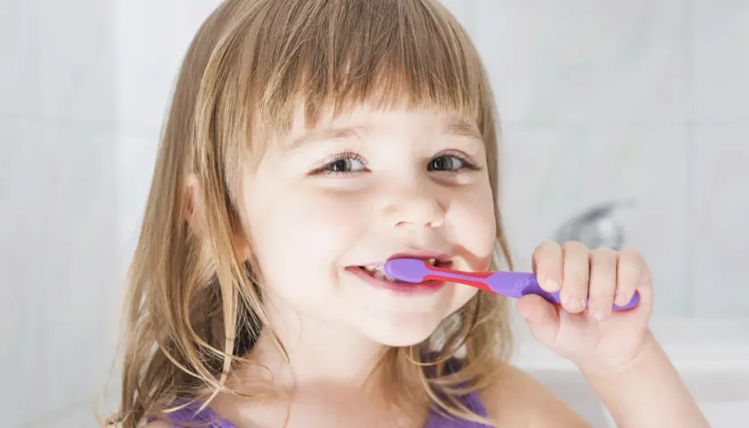 Bambina sorridente si lava i denti con un dentifricio al fluoruro di sodio per un sorriso smagliante.