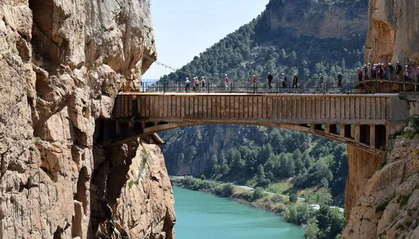 Spacerzy po wąwozie El Caminito del Rey, atrakcji, z której słynie Malaga. Widok na most nad turkusową rzeką.
