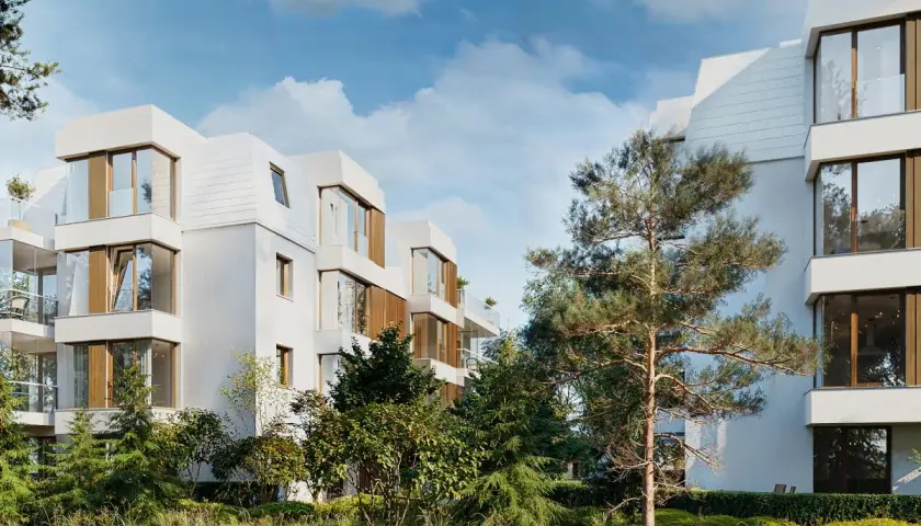 Nowoczesna sopocka architektura, białe budynki z drewnianymi elementami i dużymi oknami, otoczone zielenią.