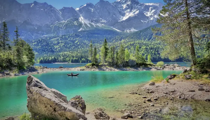 Türkiser Bergsee in Deutschland mit schneebedeckten Gipfeln im Hintergrund. Ein Kanufahrer genießt die Ruhe.