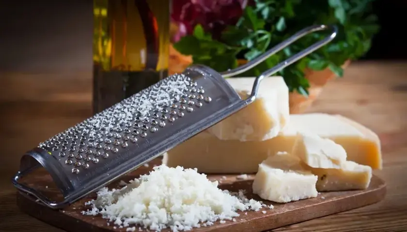 Tarka z grudkami sera, obok kawałki Grana Padano i parmezanu, gotowe do starcia.