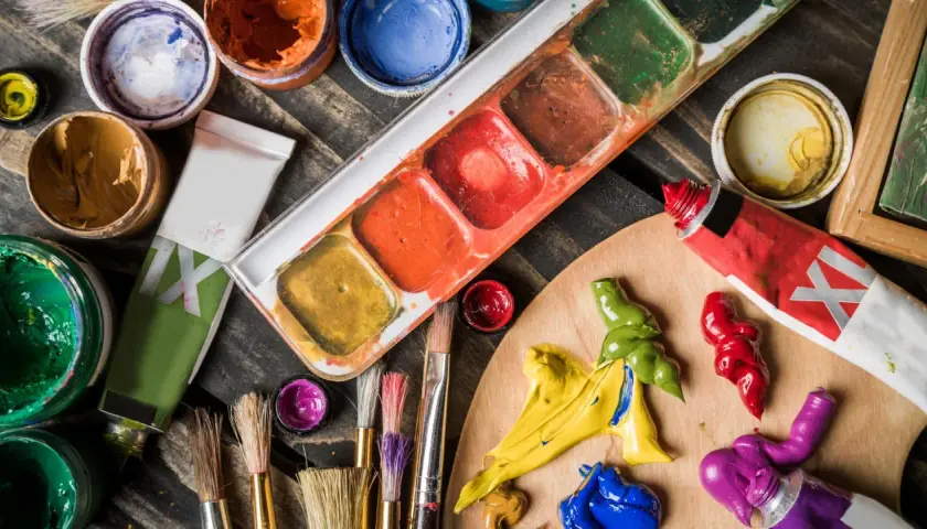 Palette d'un artiste peintre acrylique avec tubes de peinture, pinceaux et godets de couleurs vives sur fond de bois.