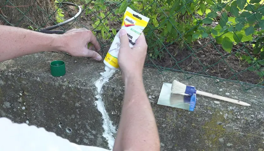 Hände dichten Betonrisse mit einer Tube ab. Ein Spachtel und Pinsel liegen bereit.