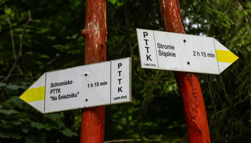 Znaki PTTK wskazują drogę do schroniska "Na Śnieżniku" (1h 15 min) i do Stronia Śląskiego (2h 15 min).