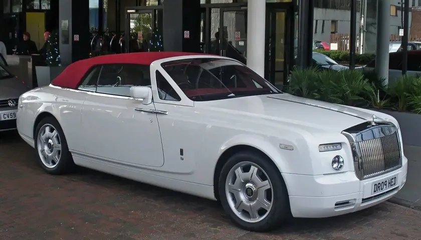 Biały Rolls-Royce Phantom Drophead Coupe z czerwoną, opuszczoną dachem, zaparkowany przed budynkiem.