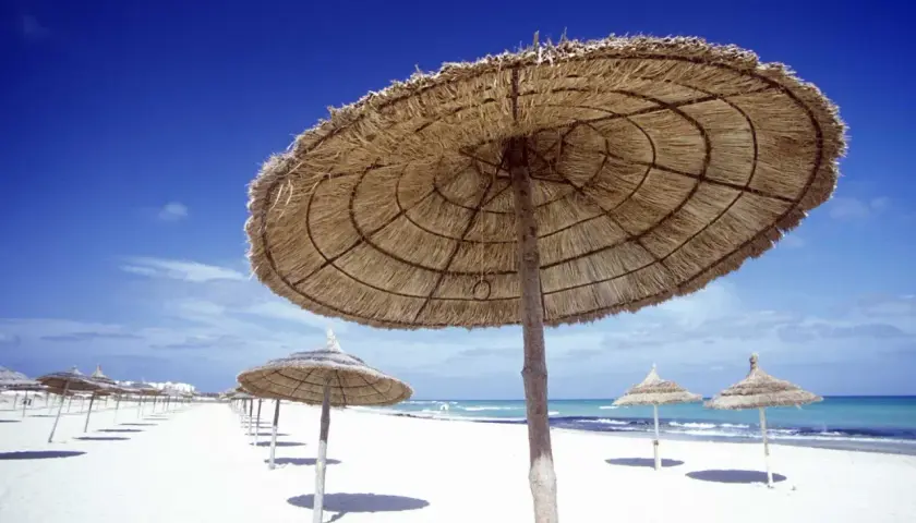 Słomiane parasole na białej plaży, idealne miejsce, kiedy do Tunezji. Błękitne niebo i morze zapraszają do relaksu.