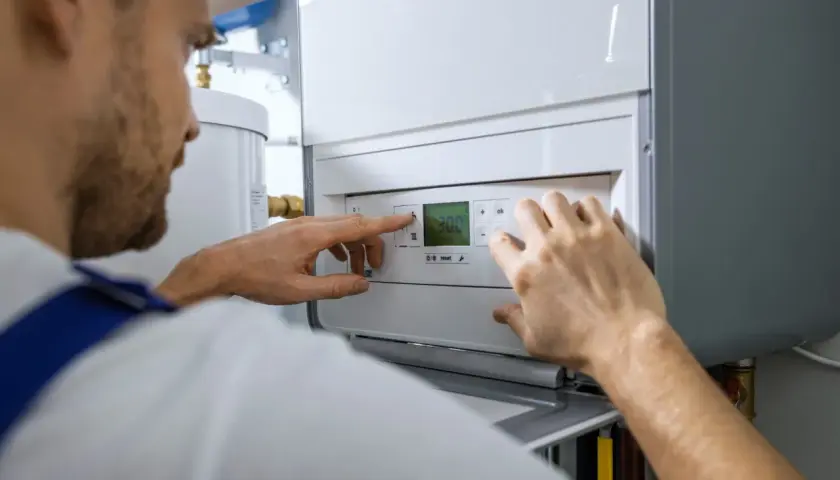 Fachowiec reguluje nowoczesną instalację gazową w domu. Na wyświetlaczu kotła widoczna jest temperatura 30.0.