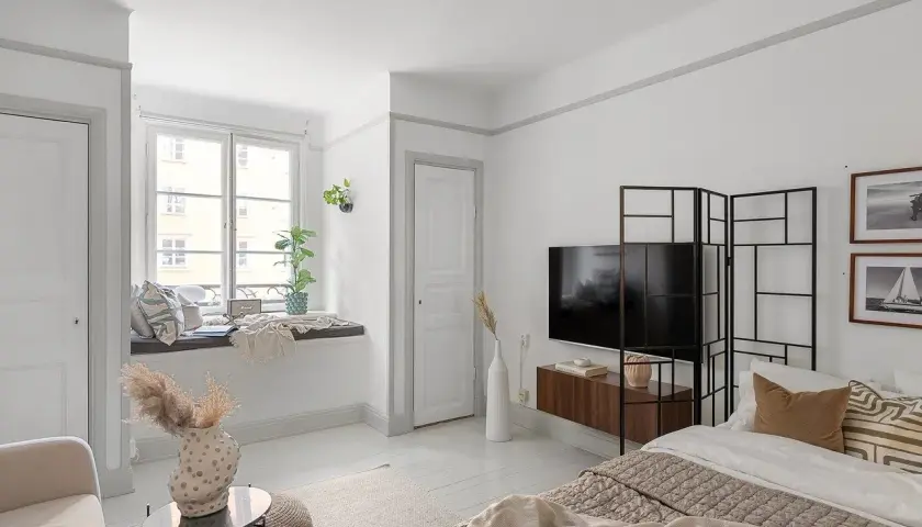 Przytulne mieszkanie bezczynszowe z wygodną kanapą przy oknie, łóżkiem i telewizorem.