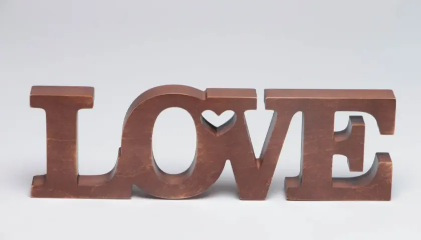 Letras de madera marrón forman la palabra "LOVE", con un corazón tallado en la "O".