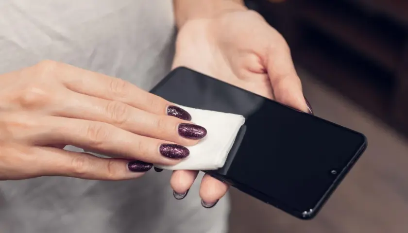 Dłoń z błyszczącymi paznokciami czyści ekran telefonu. Dowiedz się, jak wyczyścić głośnik w telefonie, by dźwięk był czysty.