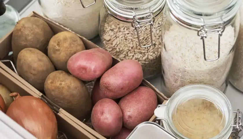 Kartoffeln lagern ohne Keller: Eine Kiste mit Kartoffeln und Zwiebeln neben Gläsern mit Reis und Haferflocken.