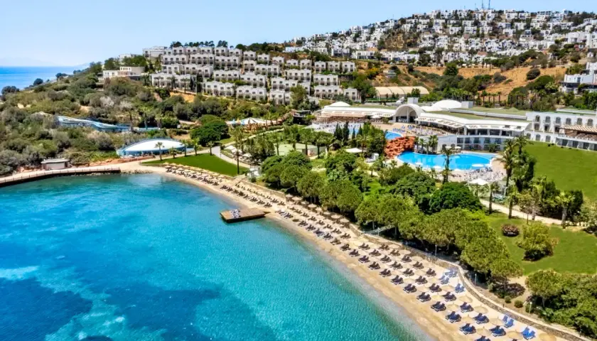 Widok na hotel Yasmin Bodrum Resort z plażą, basenami i białymi budynkami na wzgórzu. Idealne miejsce na wakacje, jak sugerują yasmin bodrum resort opinie.