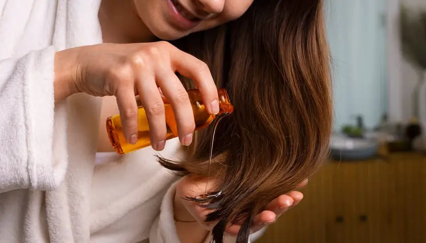 Mujer aplica aceite en su cabello. Descubre la vitamina e para que sirve en el cabello: brillo y fortaleza.