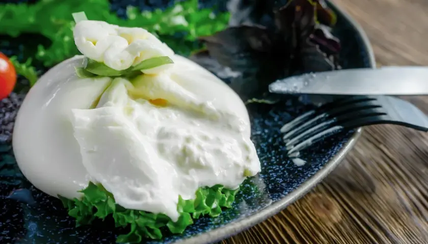 Une burrata fumée onctueuse sur un lit de verdure, prête à être dégustée. Une recette simple et savoureuse.