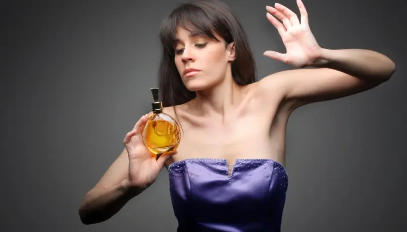 Kobieta w fioletowej sukni trzyma buteleczkę perfum.