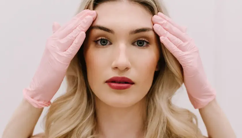 Kobieta w różowych rękawiczkach dotyka skroni, przygotowując się do zabiegu face lifting.