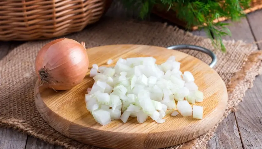 Cipolla intera e tritata su tagliere di legno. Un rimedio naturale per come togliere l'odore di aglio dalla bocca.
