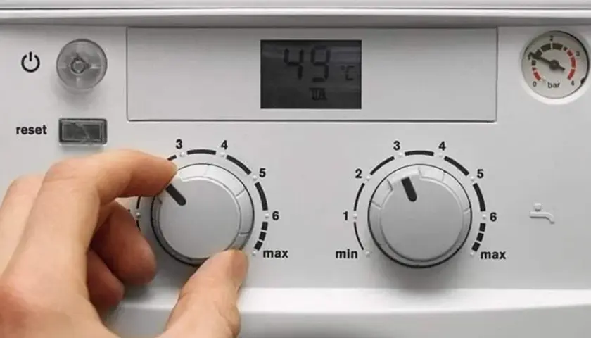 Ręka ustawia pokrętło pieca gazowego dwufunkcyjnego De Dietrich. Cyfrowy wyświetlacz pokazuje 49°C.
