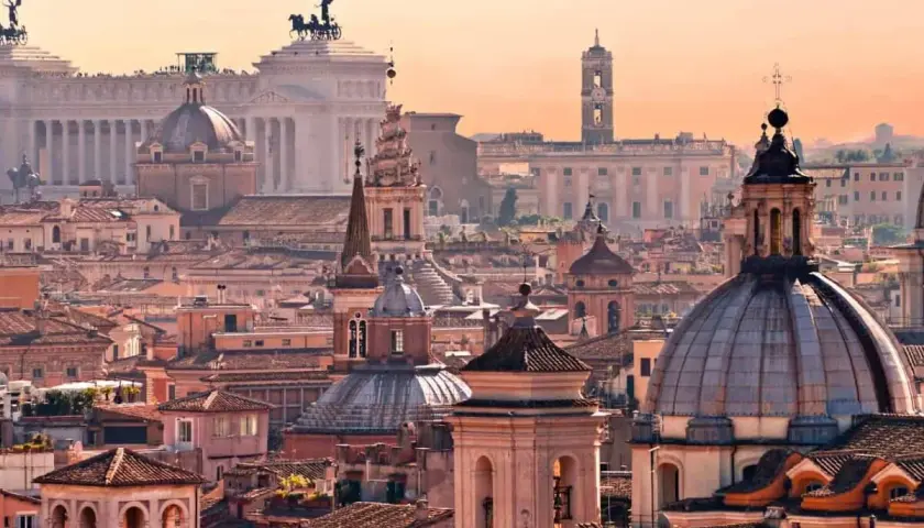 Panorama di Roma al tramonto, con cupole e monumenti iconici. Un invito a scoprire le tante cose da fare a Roma.