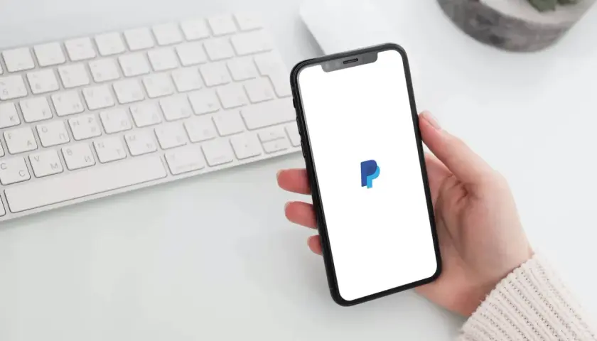 Dłoń trzyma smartfon z logo PayPal, obok klawiatura. Zastanawiasz się, czy PayPal jest darmowy?