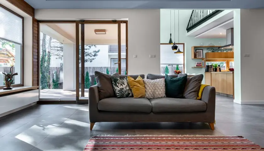 Nowoczesny salon z szarą kanapą i dywanem. Eleganckie łączenie kolorów ścian: dwa kolory ścian w jednym pokoju tworzą przytulną atmosferę.