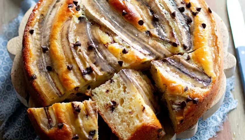Delizioso dolce con banane e gocce di cioccolato, tagliato a fette su un tagliere di legno.
