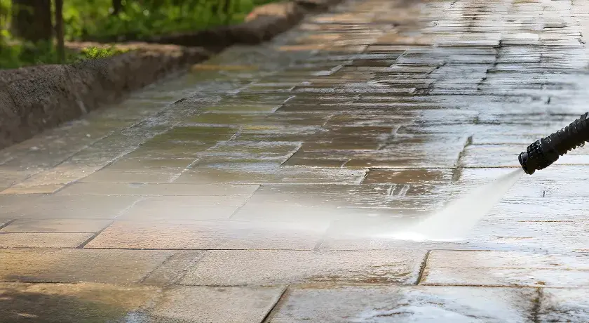 Hochdruckreiniger säubert ein Betonpflaster. Der Wasserstrahl entfernt Schmutz und lässt die Steine wieder wie neu aussehen.
