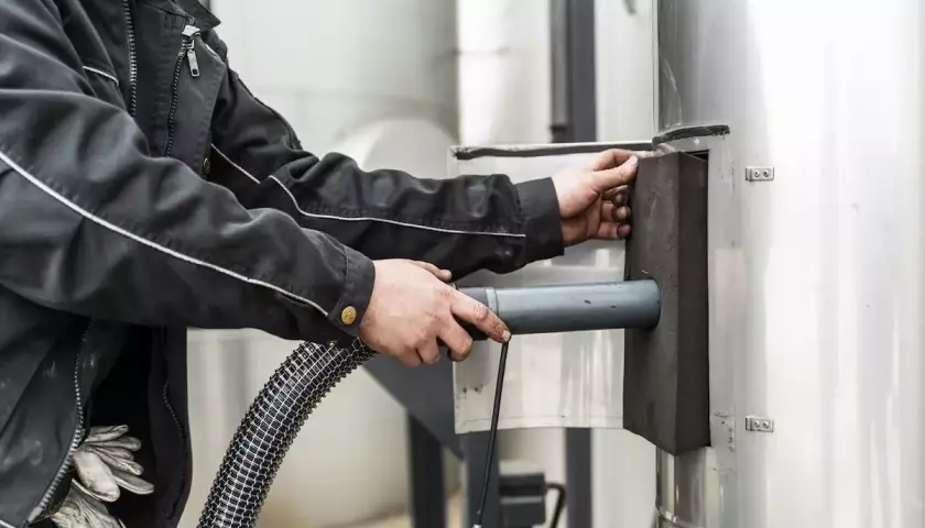 Pracownik czyści komin przez drzwi wyczystki kominowej, używając węża.