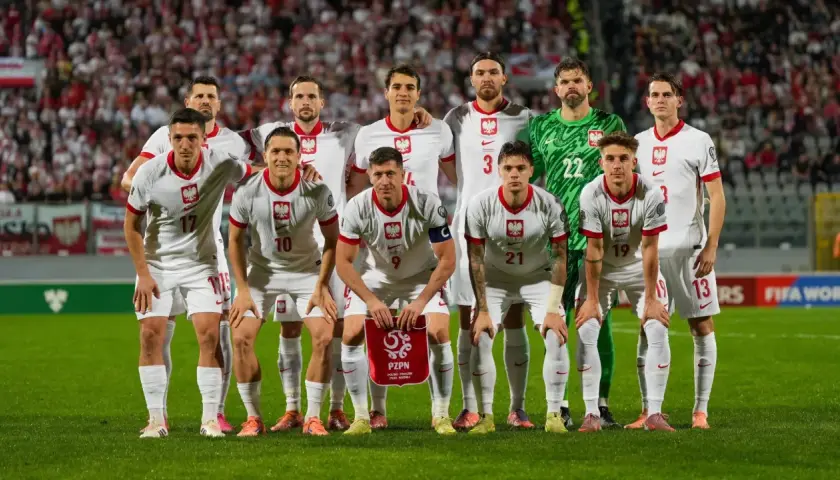 Zgrupowanie reprezentacji Polski. Piłkarze w białych strojach z orłem na piersiach pozują na tle trybun.