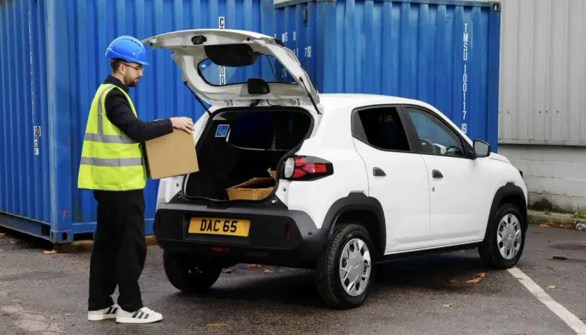 Pracownik w kamizelce odblaskowej wkłada paczkę do bagażnika białego Dacia Spring Cargo, gotowego do dostawy.