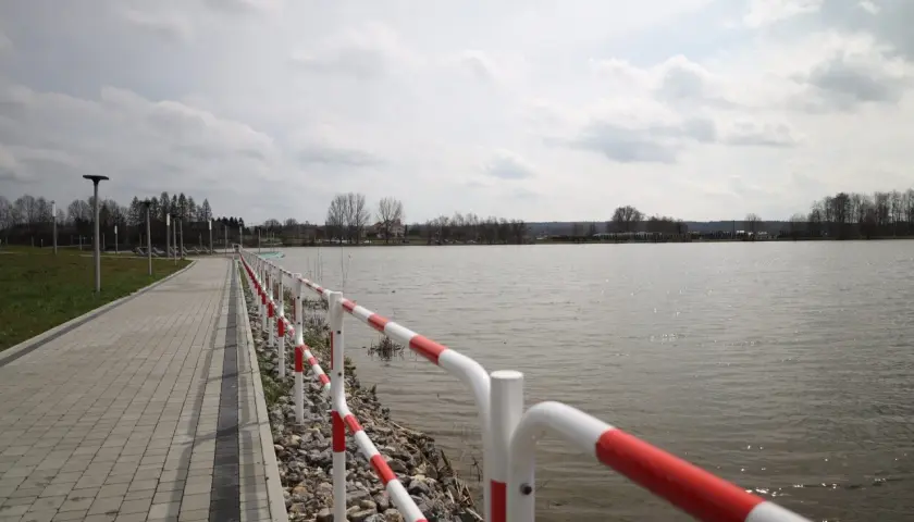 Spacerem nad zalewem wolbromskim, z czerwono-białą barierką i brukowaną ścieżką.