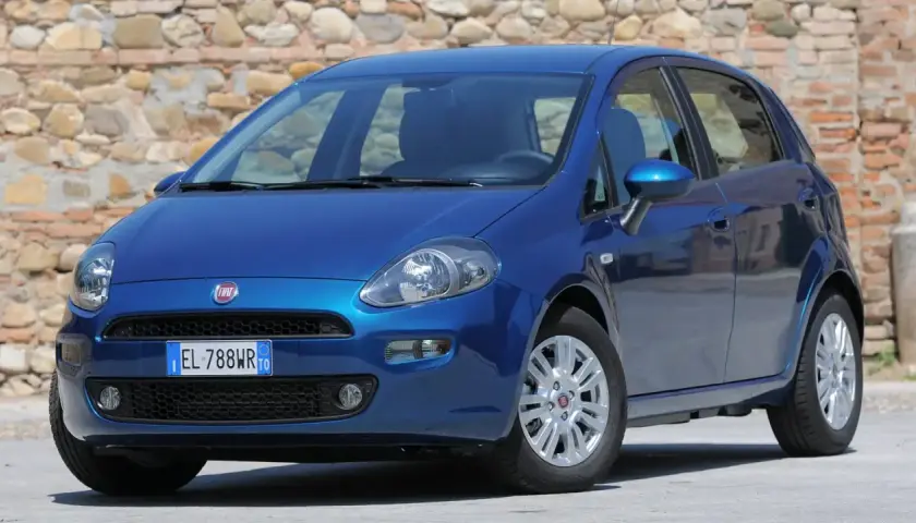 Una Fiat Punto blu brillante parcheggiata davanti a un muro di pietra.