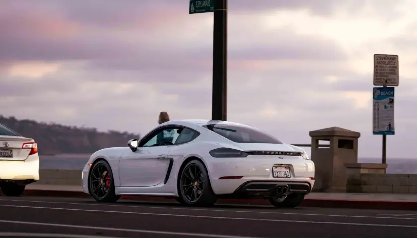 Białe Porsche GT4 z czerwonymi zaciskami hamulcowymi stoi przy drodze z widokiem na ocean.