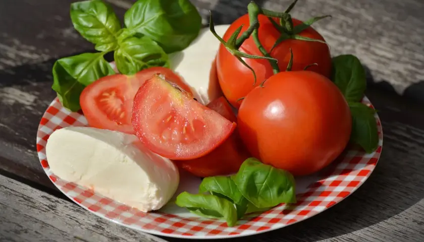 Pomidory, mozzarella i bazylia na talerzu. Czy mozzarella jest dobra na odchudzanie? To składniki lekkiej sałatki.