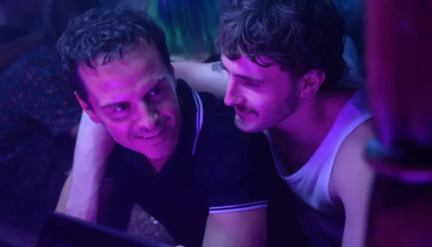 Dwóch mężczyzn w klubie, jeden z nich uśmiecha się do drugiego. To scena z filmu "Dobrzy nieznajomi", która zasługuje na recenzję.