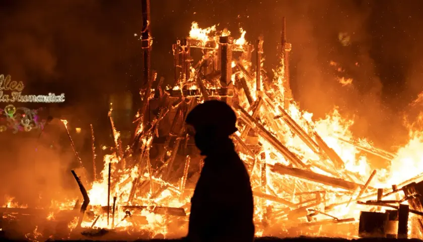 Silueta de persona observando la **cremà** de una falla en **Valencia**. El fuego consume la estructura de madera, creando un espectáculo de llamas y humo.