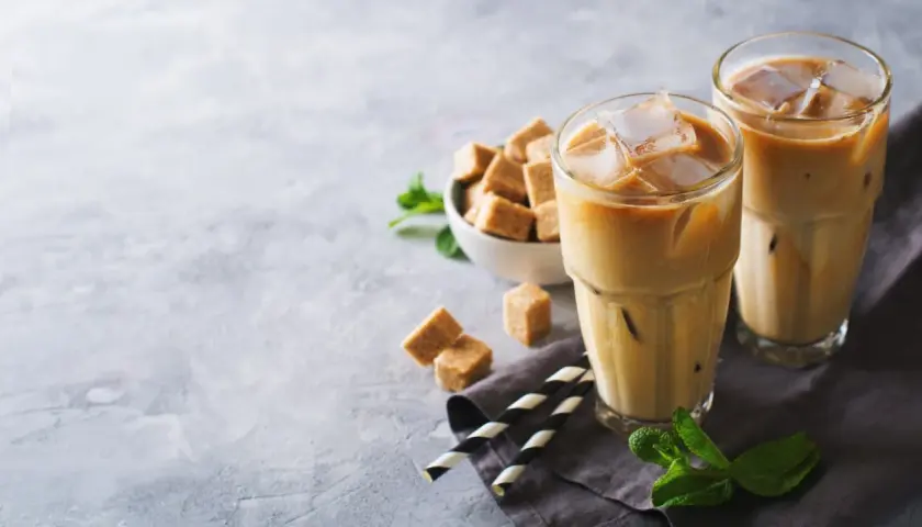 Dwa orzeźwiające freddo espresso z lodem, kostki brązowego cukru i listki mięty na szarym tle. Idealne na upalny dzień.