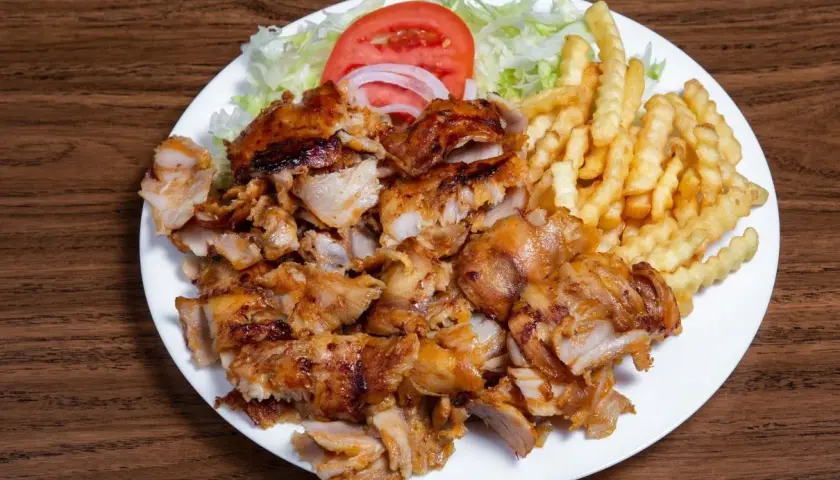 Talerz z kurczakiem gyros, frytkami, sałatą, pomidorem i cebulą.