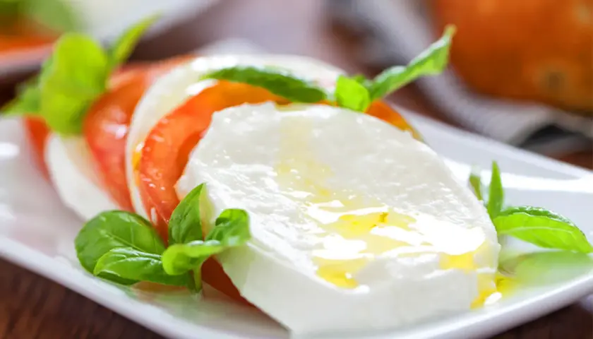 Frische Insalata Caprese mit saftigen Tomaten, cremigem Mozzarella und Basilikum, beträufelt mit Olivenöl. Ein Genuss!