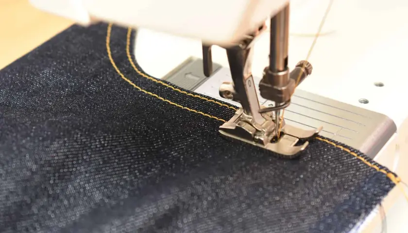 Close-up of a sewing machine stitching dark denim with yellow thread. Perfect sewing machine settings for denim are key for strong seams.