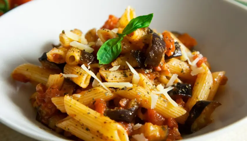 Penne z bakłażanem i pomidorami, posypane parmezanem. Proste danie włoskie, które zachwyca smakiem.