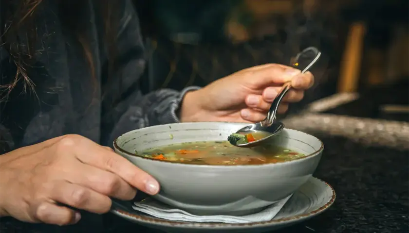 Gorący bulion warzywny na łyżce, idealny, gdy zastanawiasz się, co jeść przy gorączce.