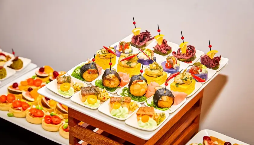 Elegancki catering urodzinowy Warszawa: kolorowe przekąski, sushi, tartaletki i owoce morza na białych talerzykach.