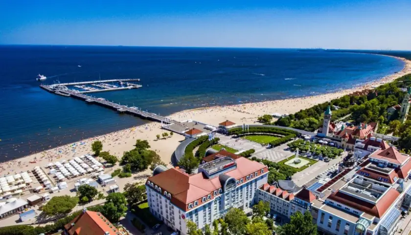Widok na fajny hotel nad morzem, z plażą pełną ludzi i molo.