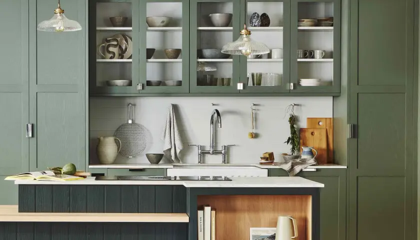 Stylish glass cabinet decor ideas in a modern kitchen with green cabinetry, showcasing ceramic bowls, plates, and glassware.