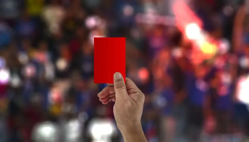 Dłoń trzyma czerwoną kartkę. Ile żółtych kartek może dostać zawodnik, zanim zobaczy tę?