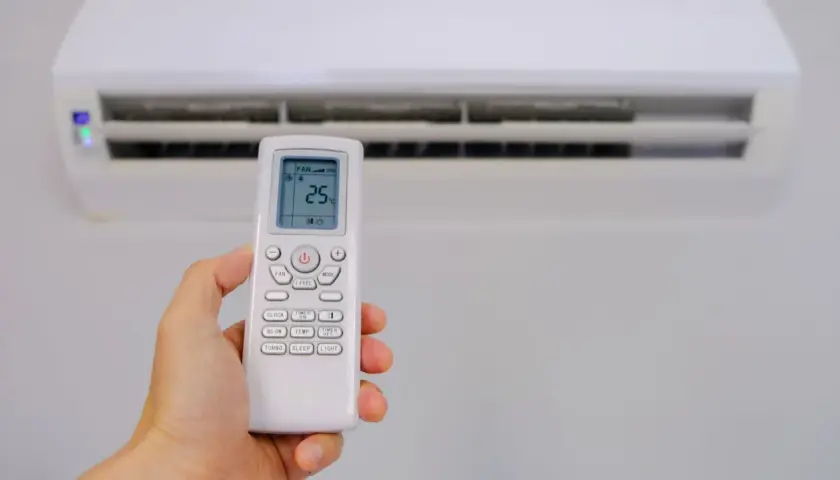 Mano sujetando control remoto de aire acondicionado, mostrando el símbolo deshumidificador aire acondicionado en pantalla.